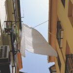 A low view of a narrow street with a white sheet blowing between the buildings