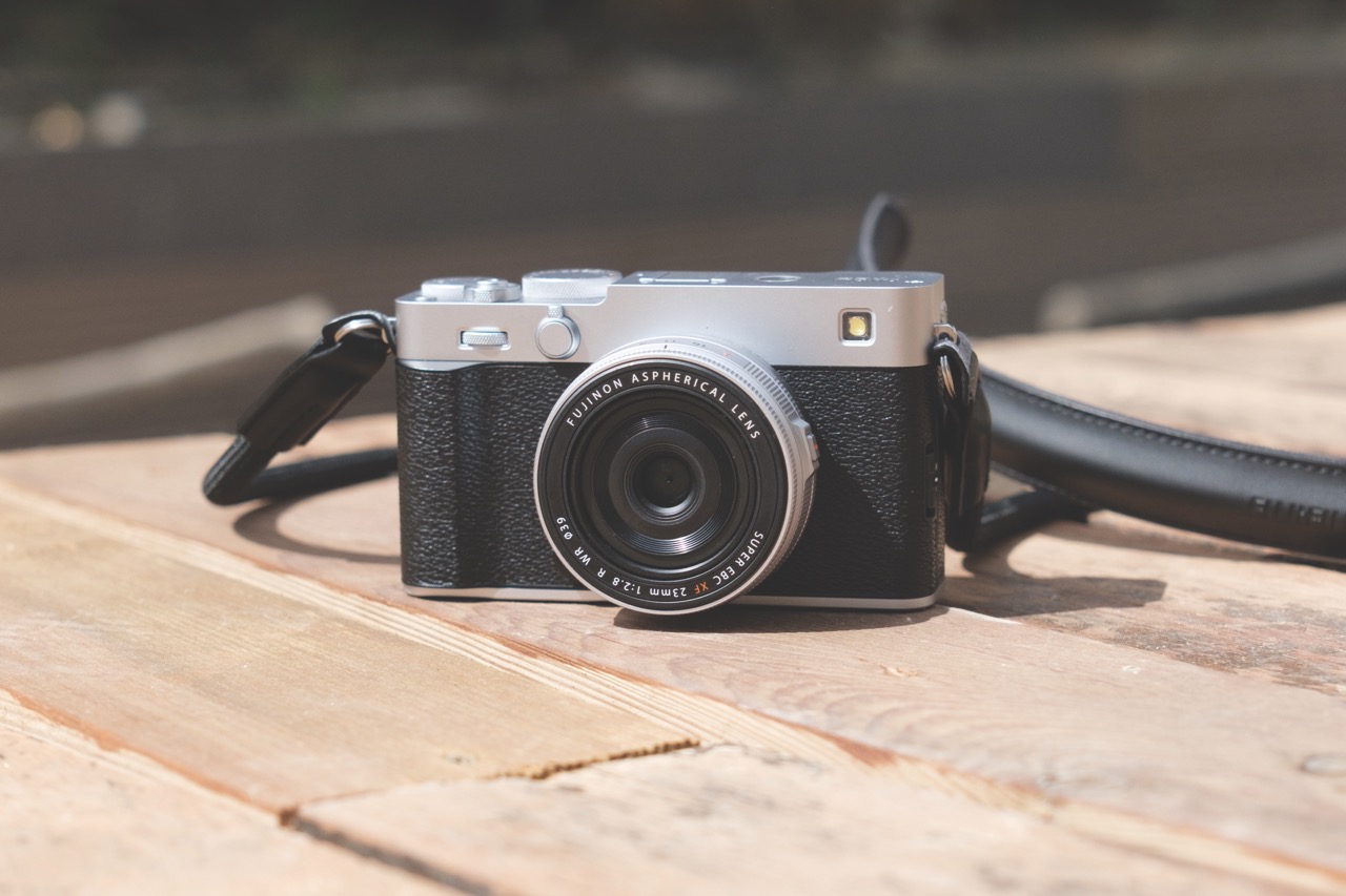 A black and silver Fujifilm camera sits on a wooden table outside