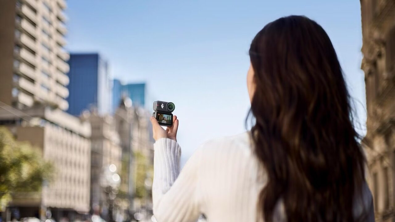Over the shoulder of a woman holding a small camera by DJI as she shoots a cityscape