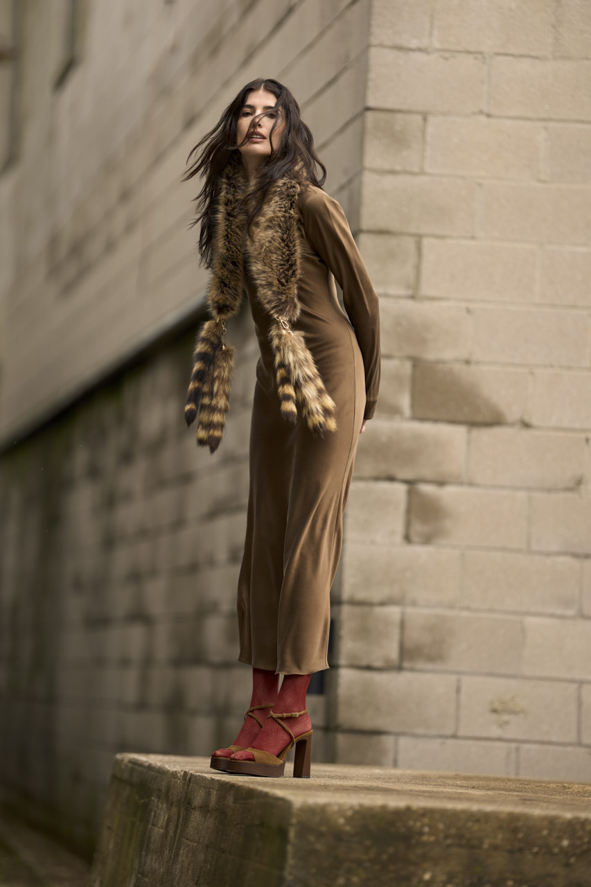 A portrait photo of a woman in brown clothes standing at a street corner
