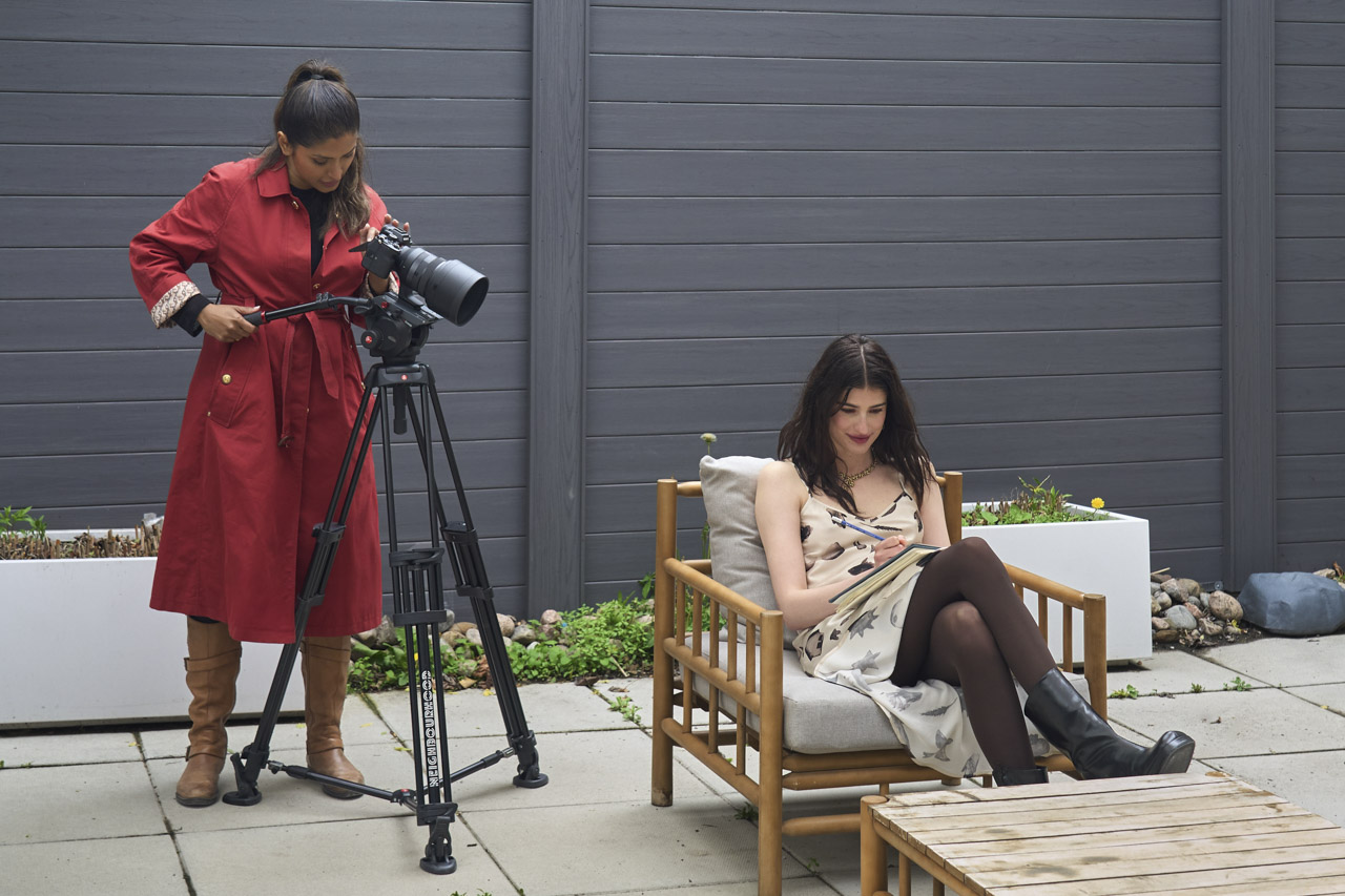A woman in a red dress adjusting a camera with a Sigma lens attached. She films another woman sitting on outside seating