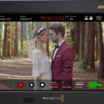 A Blackmagic Design monitor showing a photo of a man and woman standing in a forest, about to kiss