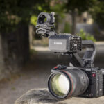 A Canon camera with multiple attachments, sitting on a stone surface in an alleyway