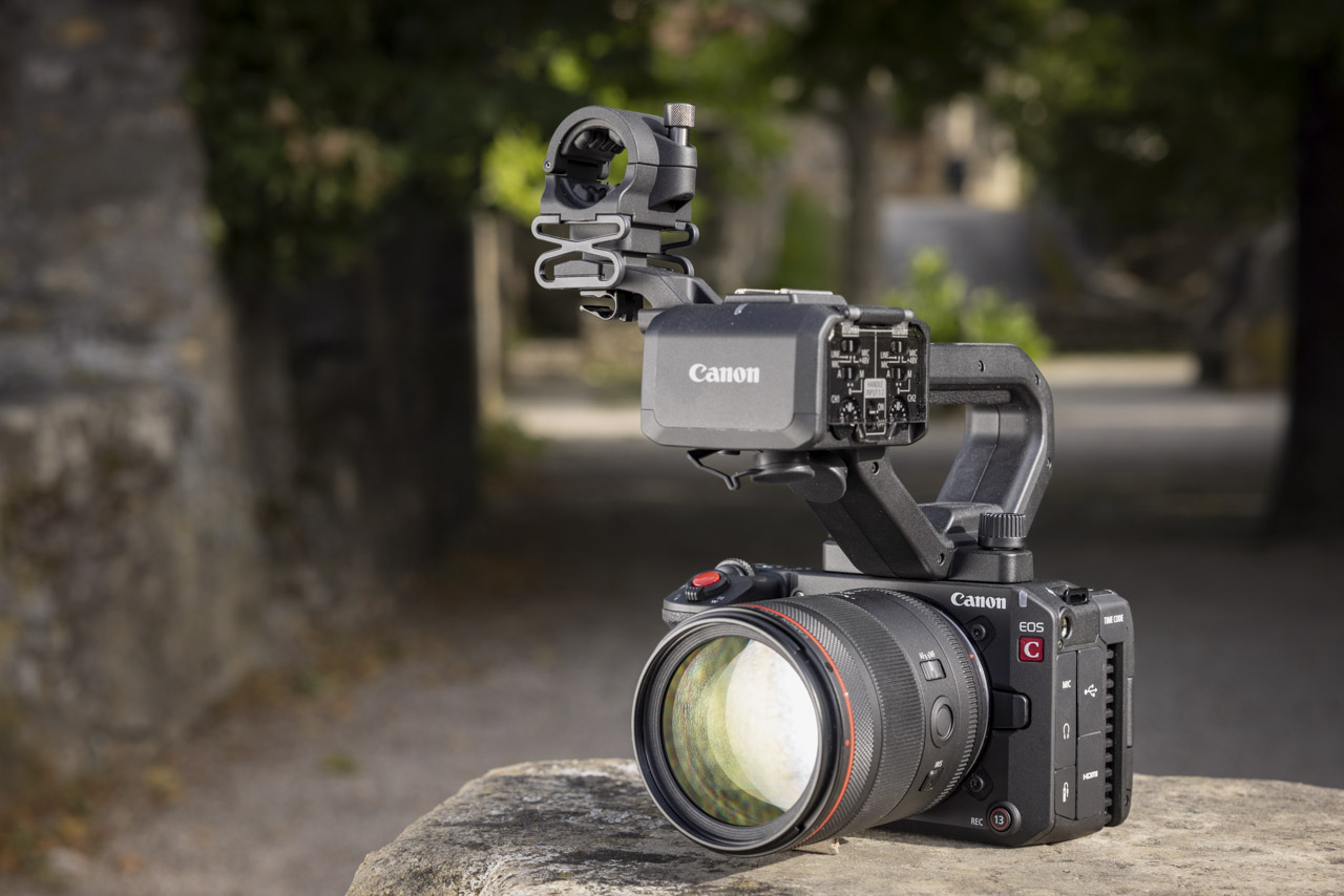A Canon camera with multiple attachments, sitting on a stone surface in an alleyway