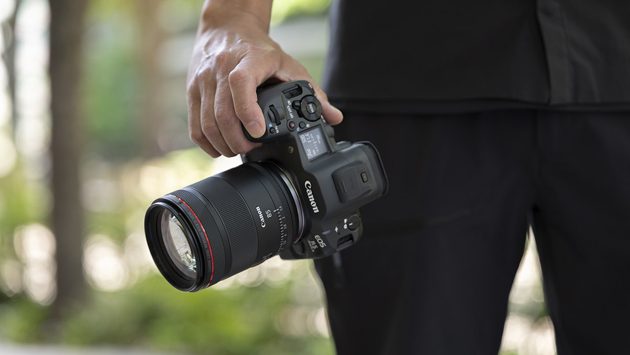 A hand holding a Canon camera by their side as they walk outside