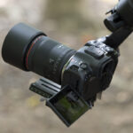 A person holding a camera with a Canon lens, using a mount