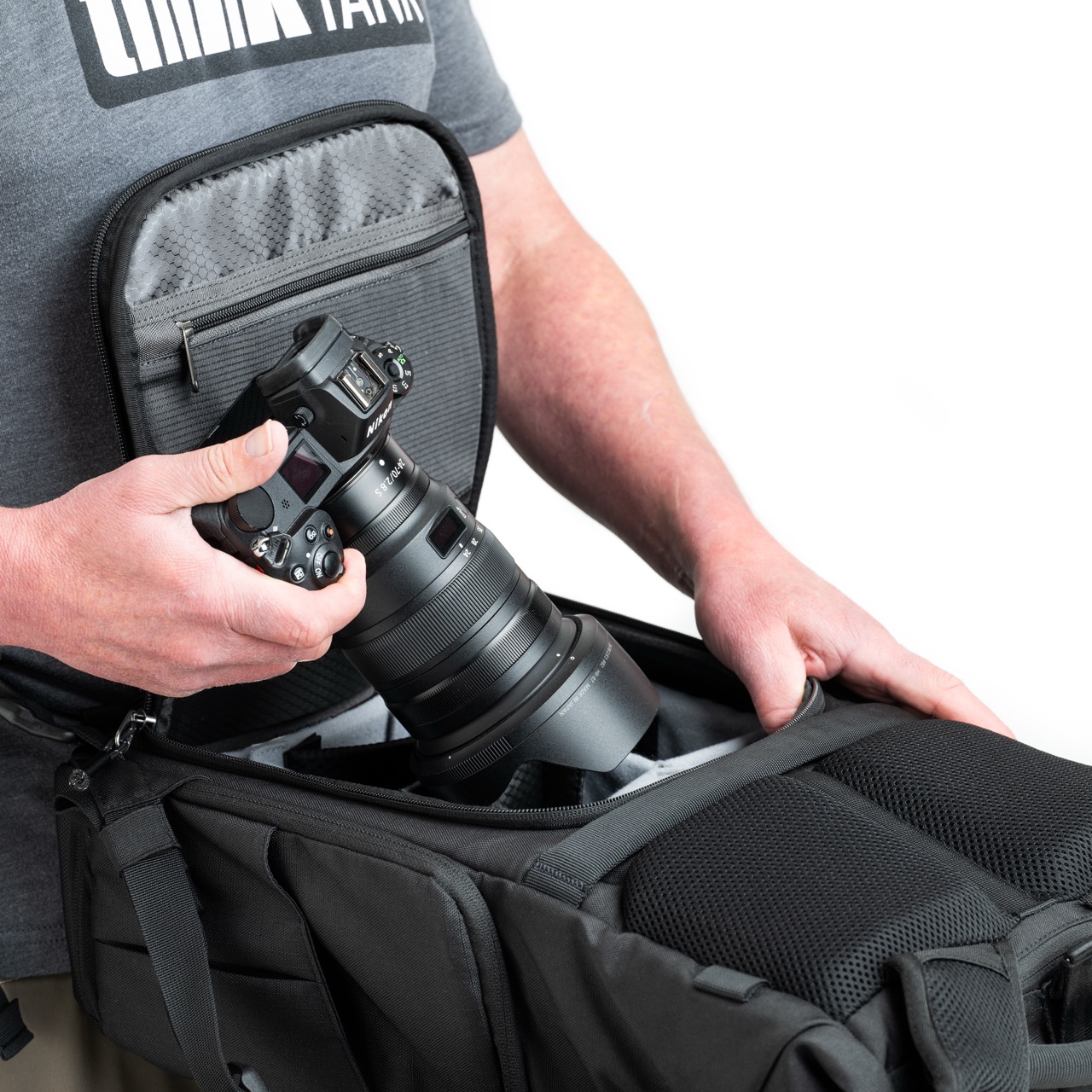 Top of a black bag from Think Tank Photo. A pair of hands is placing a camera into the top of the bag