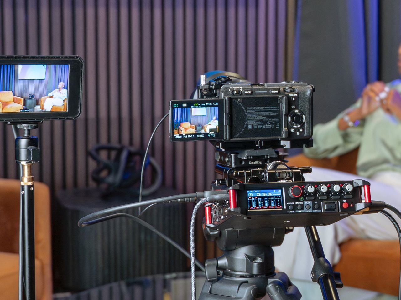 A camera on a tripod with a recording device from Tascam set up. It is placed in a living room