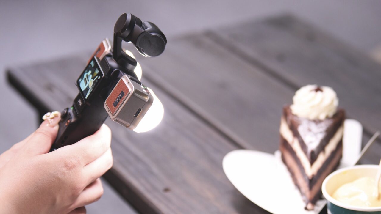 A hand holding a small light on a stick, shining onto plates of cake and coffee