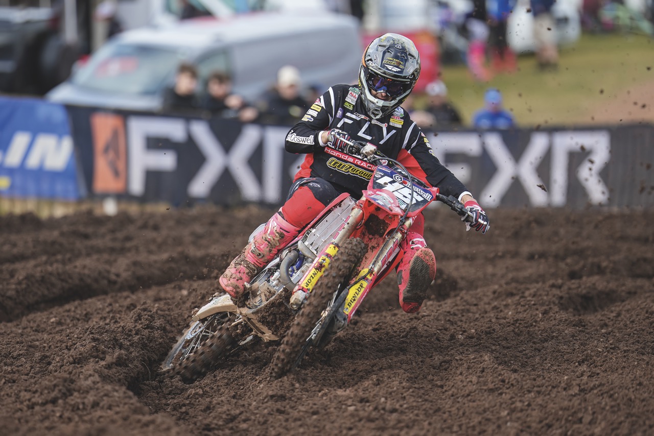 A person riding a red motorcycle in a dirt field as people look on from the sidelines