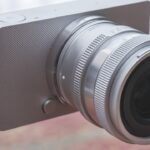 A very simple silver camera from Sigma, sitting on a transparent surface