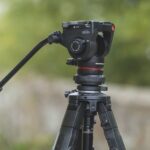 The top of a tripod from Manfrotto sitting outside on a pathway