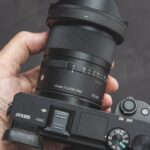 A hand holding a camera with a black Sigma lens attached