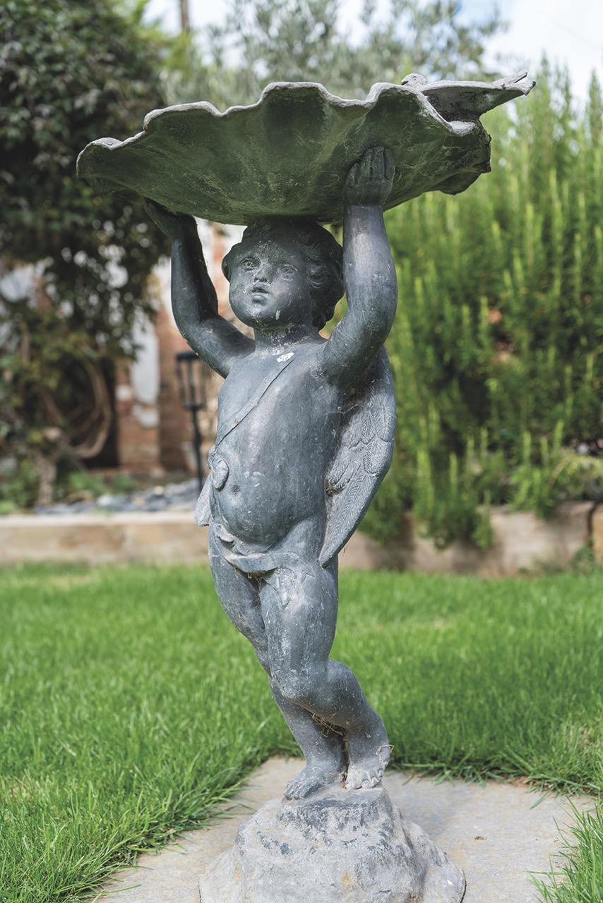 A blue statue of a cherub holding a shell above its head in a green garden