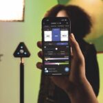 A person holding up a phone showing the Datacolor app. The phone covers a model standing in a studio