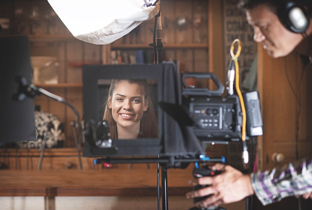 A person operating a camera, showing a smiling girl on the screen