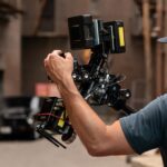 A man in a cap operating a professional camera in a street