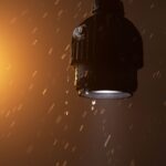 A light from Astera hanging from a loop with another light casting an orange glow behind. Rain falls from the ceiling