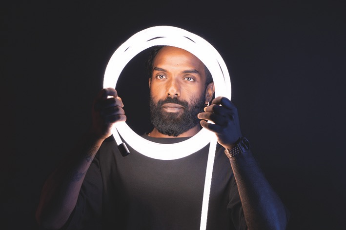 A man holds a circular light from Atomos up to his face, against a black background