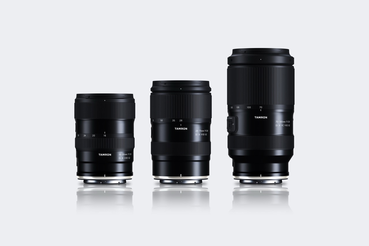 A row of lenses from Tamron standing vertically, against a shiny white background