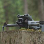 A grey DJI drone sitting on a tree stump in a forest