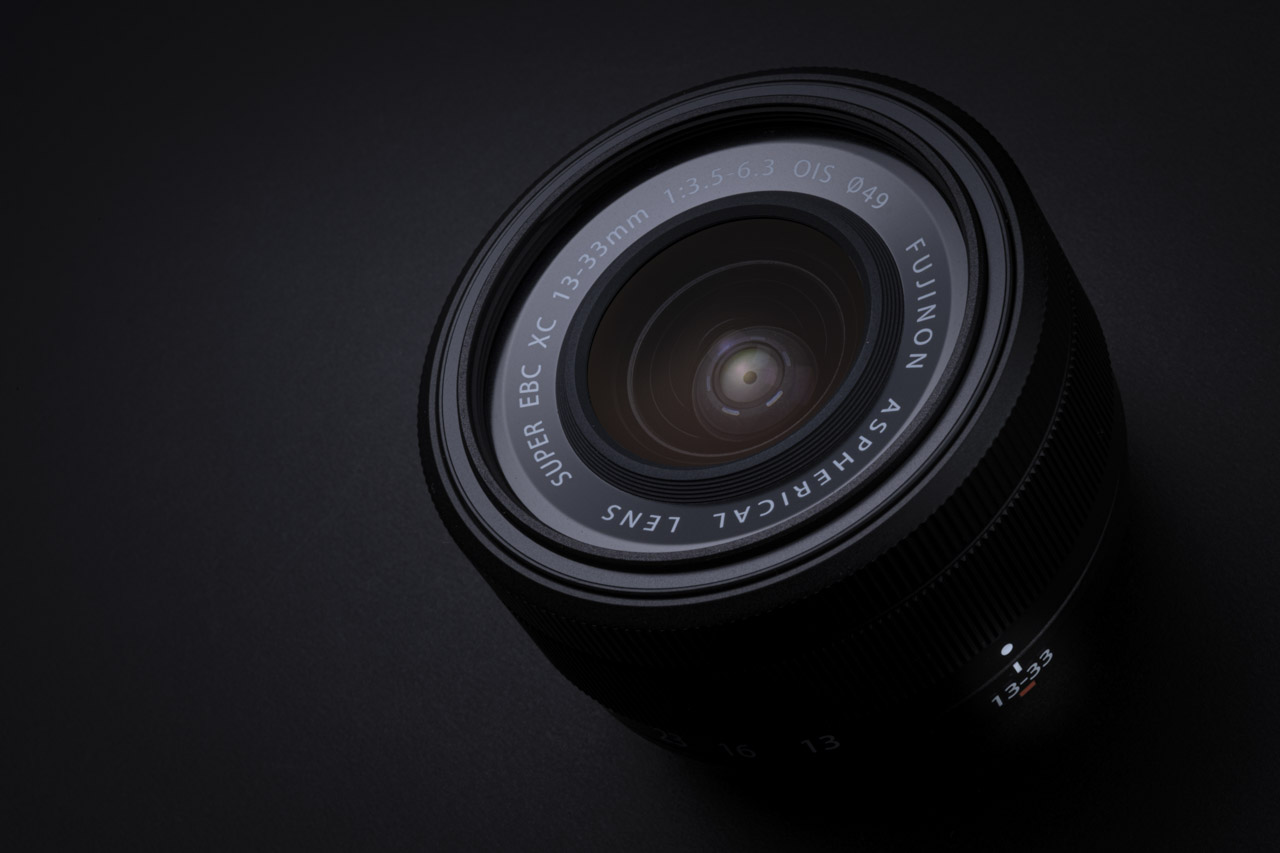 Close-up of a black Fujifilm lens, against a black background