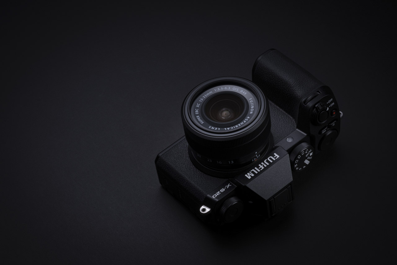 A black Fujifilm camera with a lens attached laying on its screen, against a black background