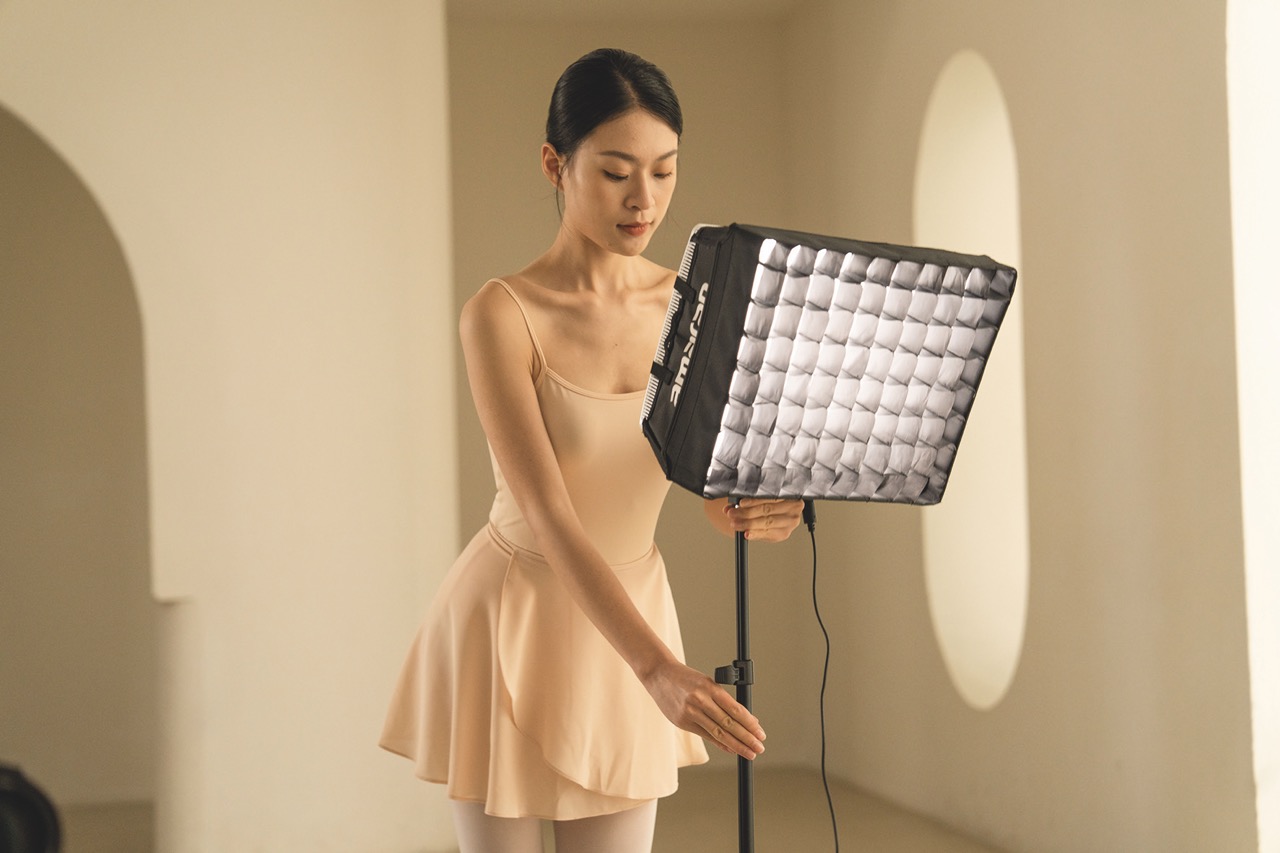 A ballet dancer adjusting a rectangular light from Amaran in a beige dance studio