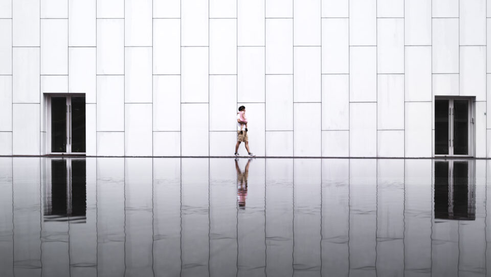 A person walking next to a pool filled with flat water and beside white walls