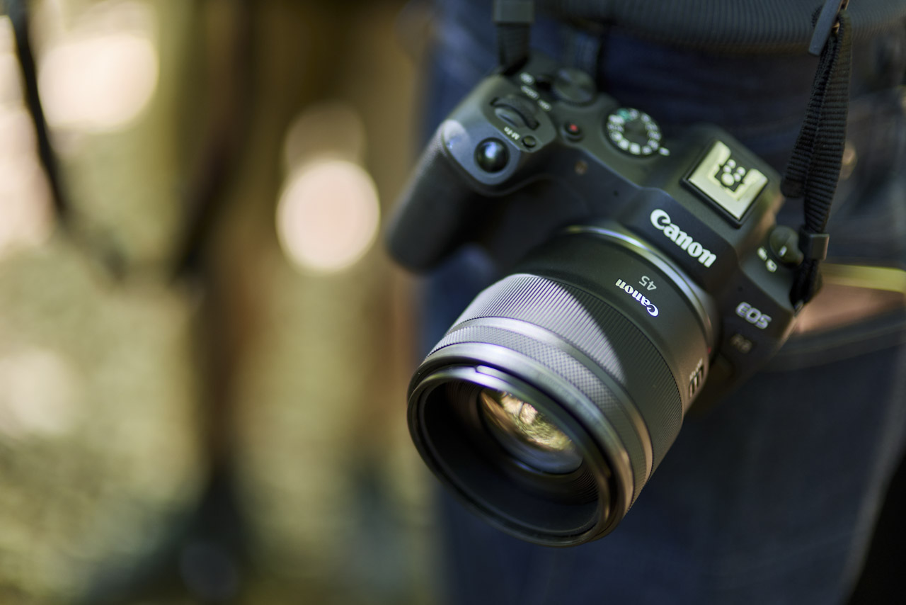 A Canon camera with a lens attached, hanging from a strap by someone's side