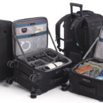 A collection of black suitcase bags from Tenba, with some upright and some open, against a white background