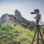 A camera attached to a tripod and placed on a green mountain