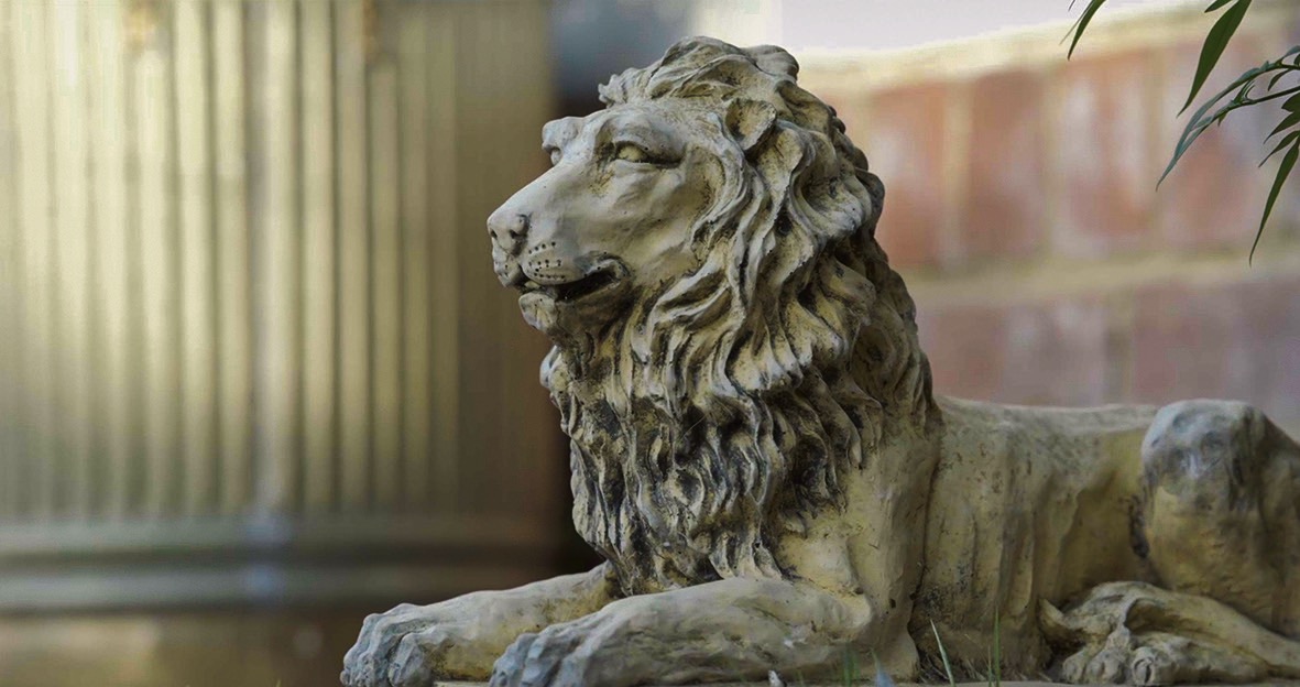 A stone lion in front of a column and brick wall