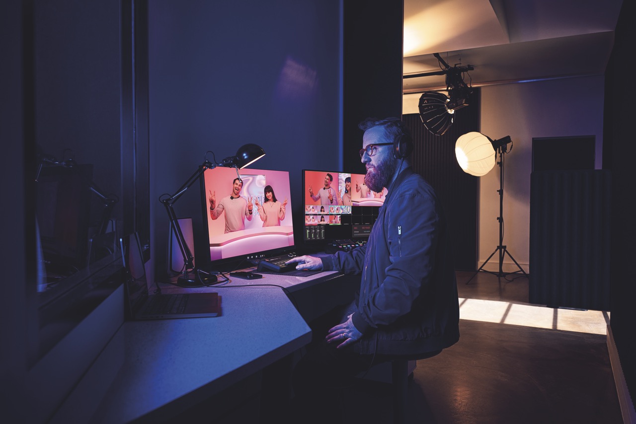 A person sitting in dark blue lighting while working on multiple monitors on a desk