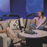 Two content creators sitting on a large sofa with Rode microphones as they create a podcast
