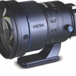 A black professional lens by Laowa placed on a stand, against a white background