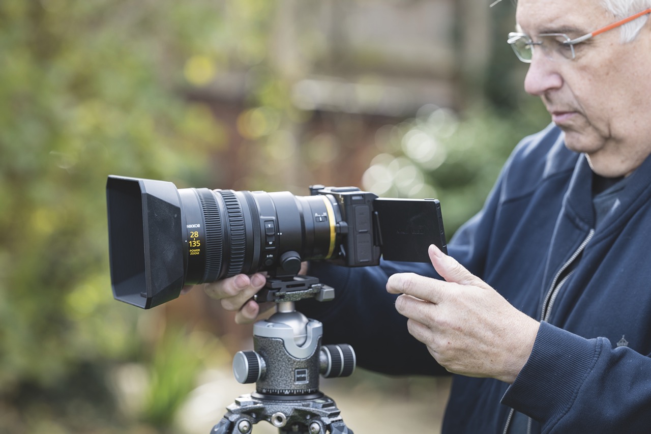 The ZR is dwarfed by the new zoom lens A man operating a cine camera from Nikon, against a blurred green background