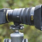 A large cine lens from Nikon, placed on a tripod, with a blurred green background