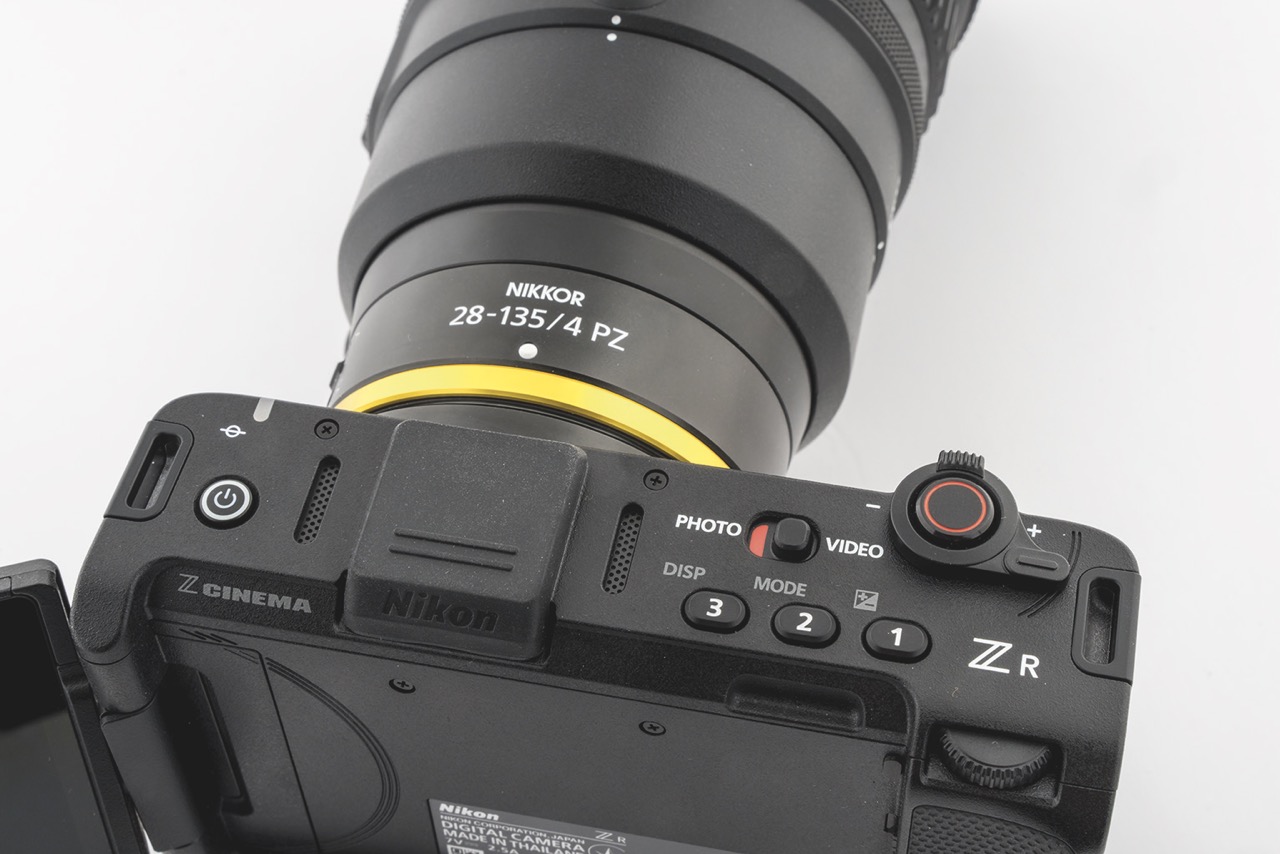 A sliding button swaps between stills and cine modes Top view of a Nikon cine camera with a yellow rim, showing the buttons on the top