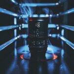 A lens from Sir with trails of blue smoke around it as it sits between pipes