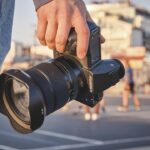A handle holding a Fujifilm camera with a blurred urban background