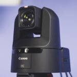 A black PTZ camera from Canon in front of a purple background