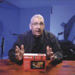 A man sits at a table in a blue room with a box from Ninja in front of him