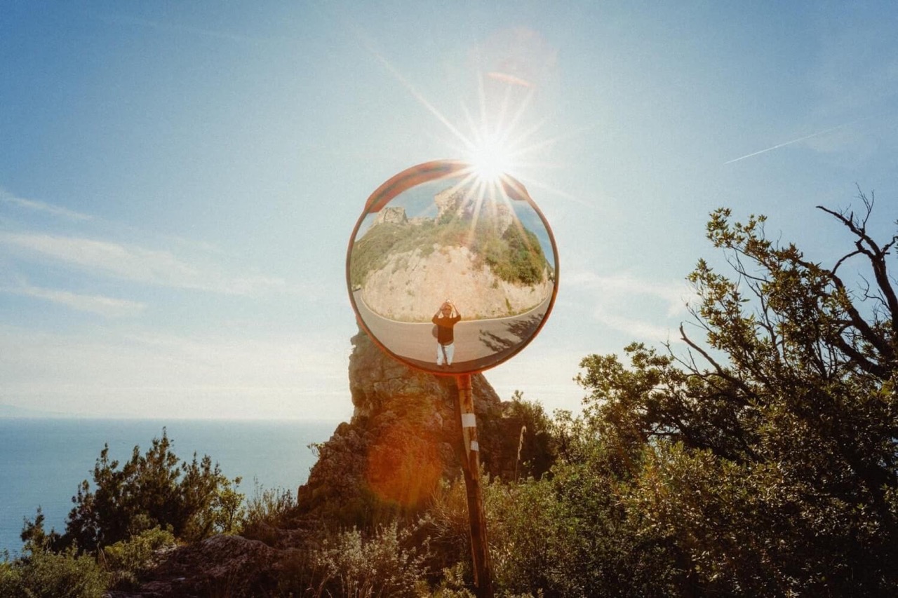 Sun glaring over the edge of a round mirror. A person takes a photo in the reflection of this mirror