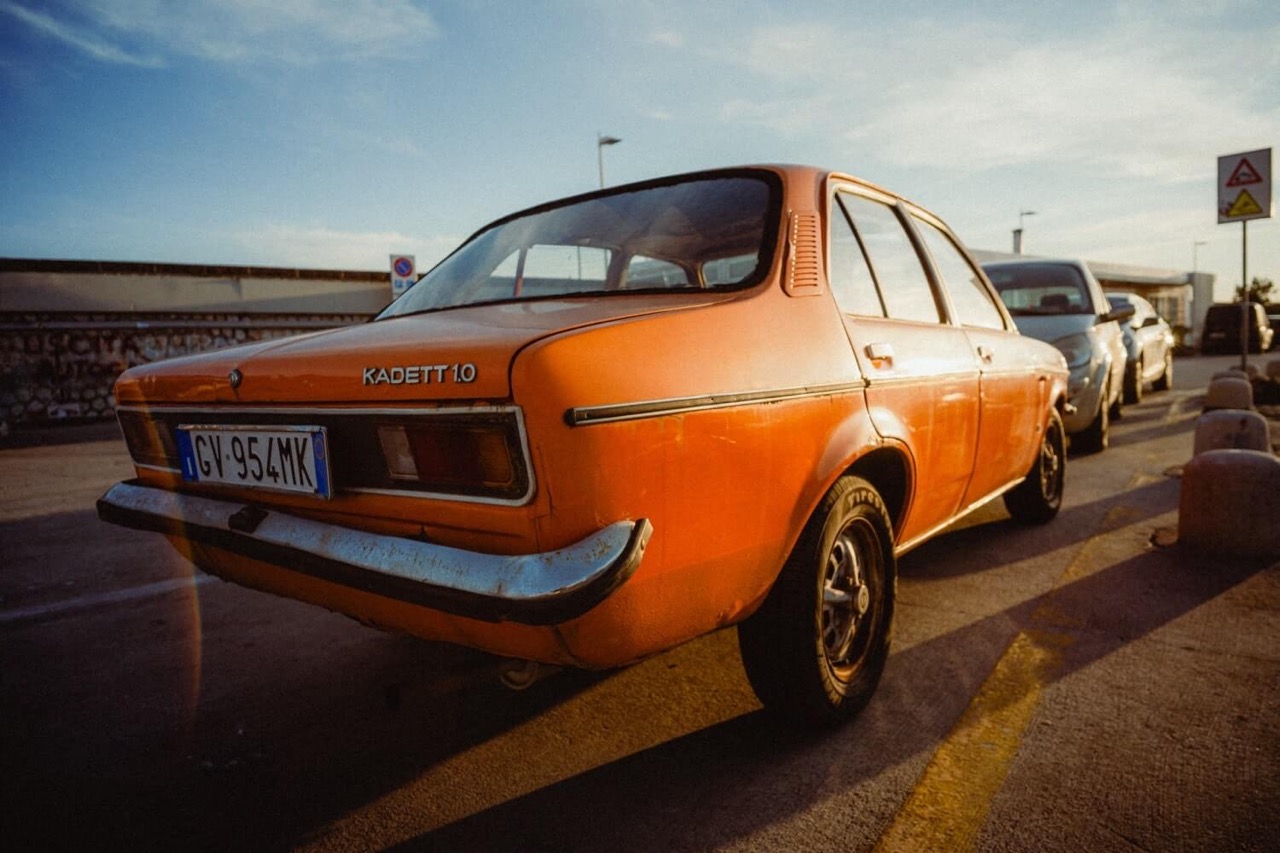A vintage image of an orange car parked on the side of a road