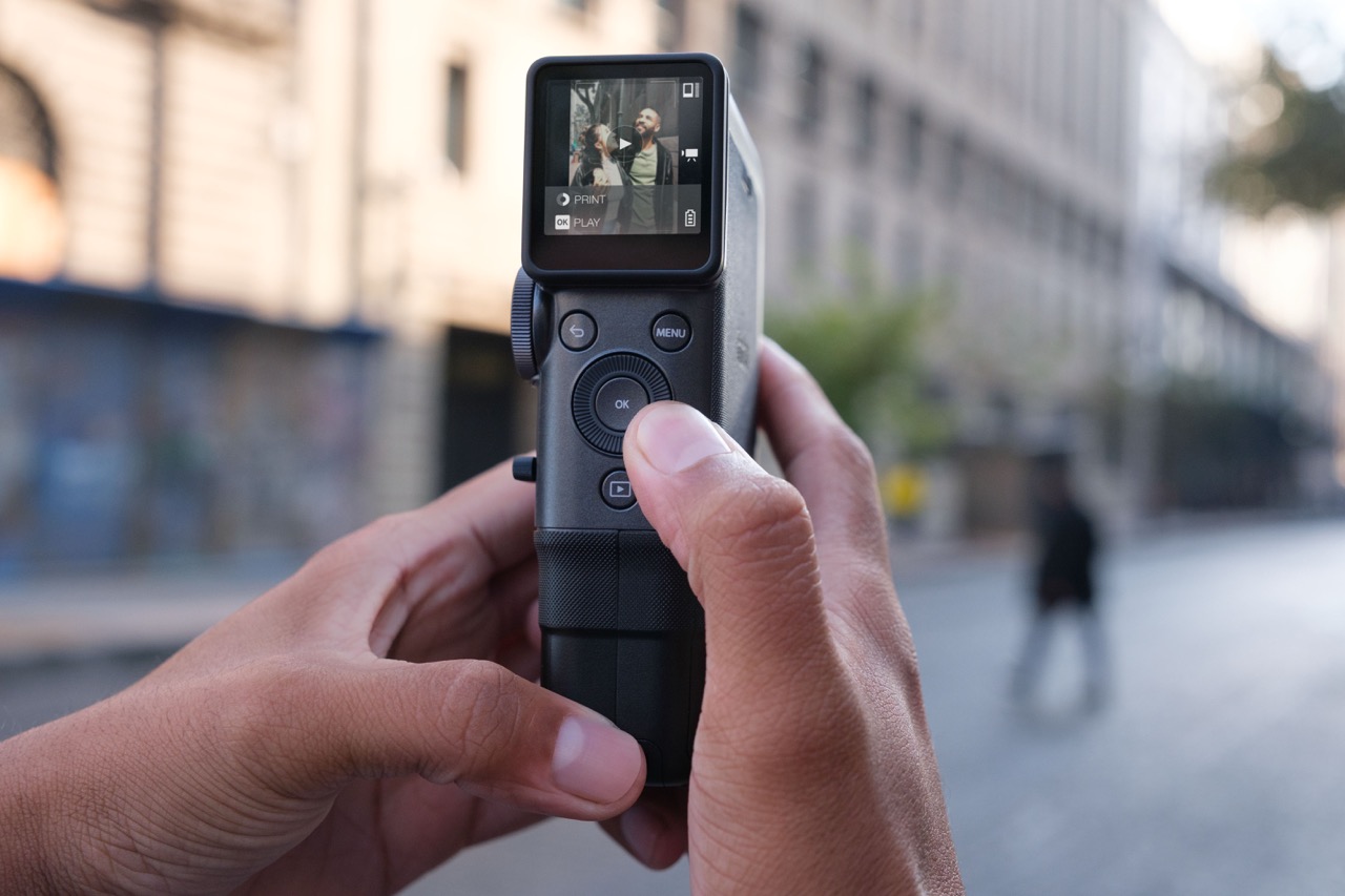 Pair of hands adjusting a dial on a Fujifilm camcorder as they stand in a city street