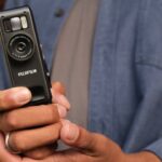 A pair of hands holding a Fujifilm camcorder