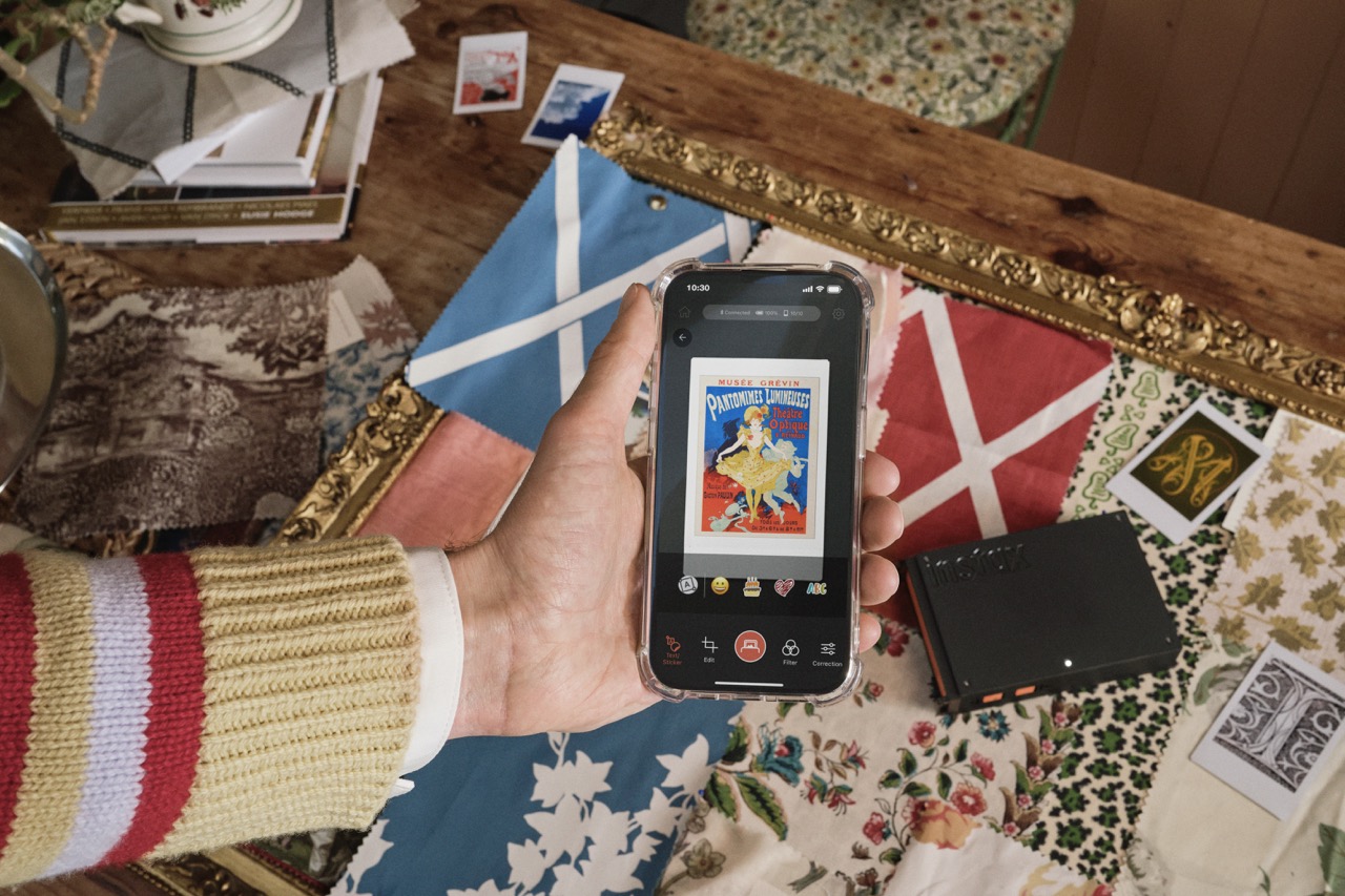 A hand with a stripy jumper holding a photo, which is scanning a print on a table