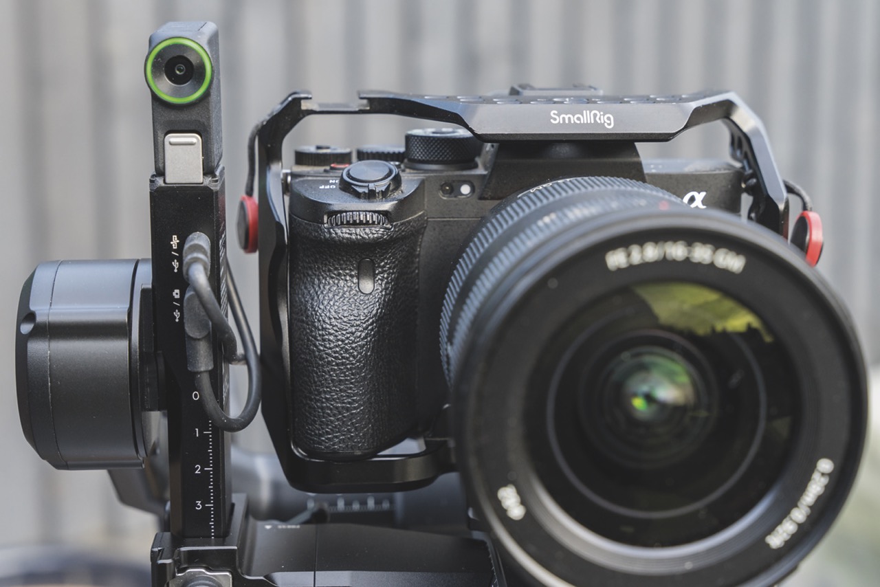 Close-up image of a camera attached to a DJI gimbal, against a wooden fence