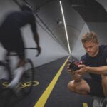 A man crouched in a tunnel, photographing a blurred cyclist